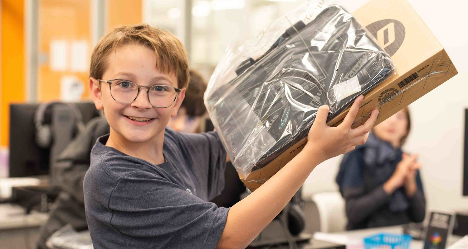 A teenage boy holding up the Chromebook he received by participating in the Coding 101 program