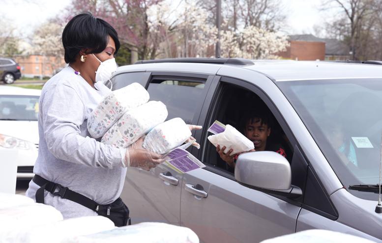 A staff member handing a pack of diapers to a resident sitting in the front passenger seat of a silver minivan