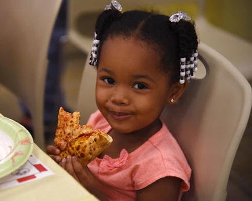 Young black girl smiles cutely while holding a piece of pizza